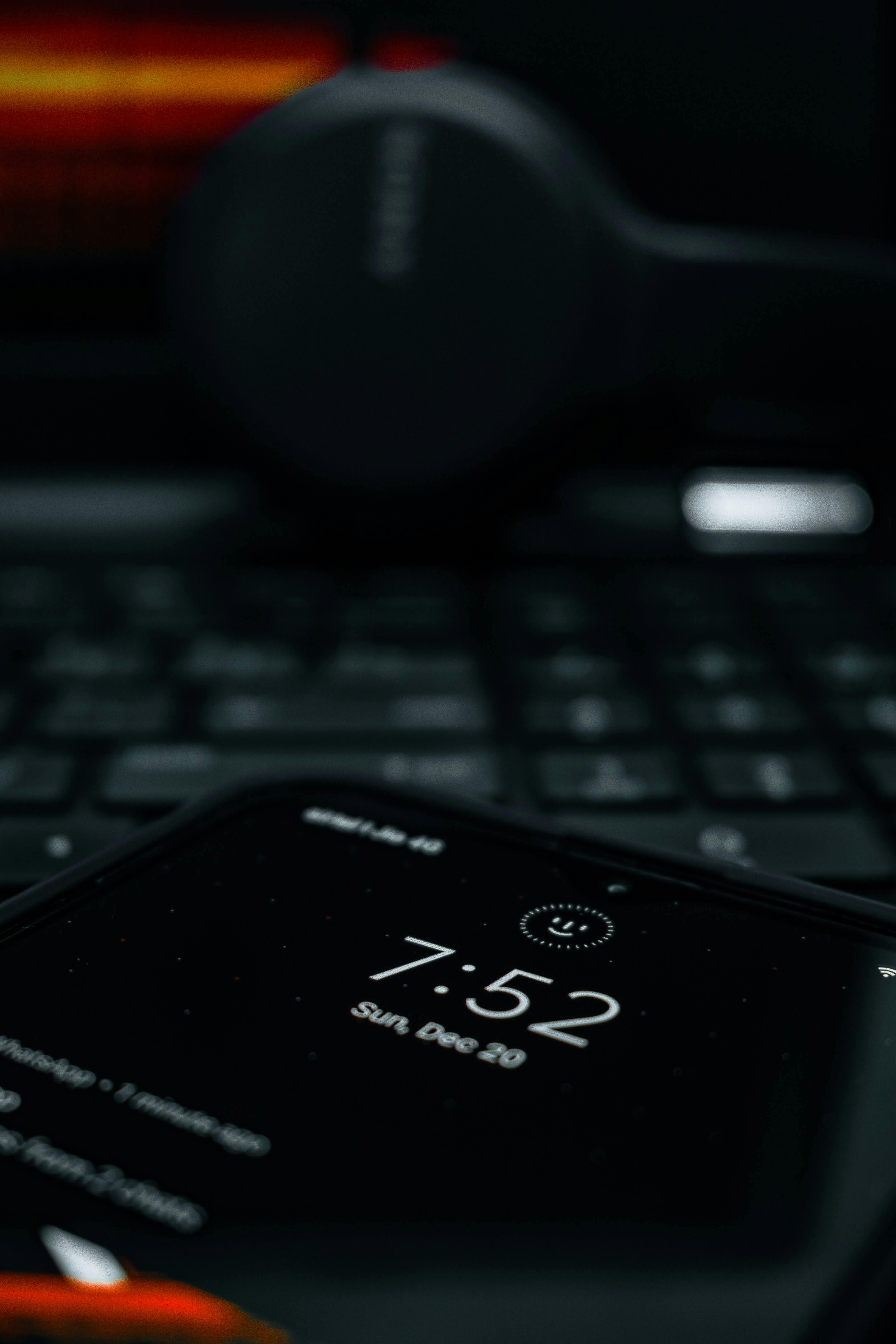 Free A smartphone showing time with a blurred laptop and headphones in the background, creating a tech-focused scene. Stock Photo