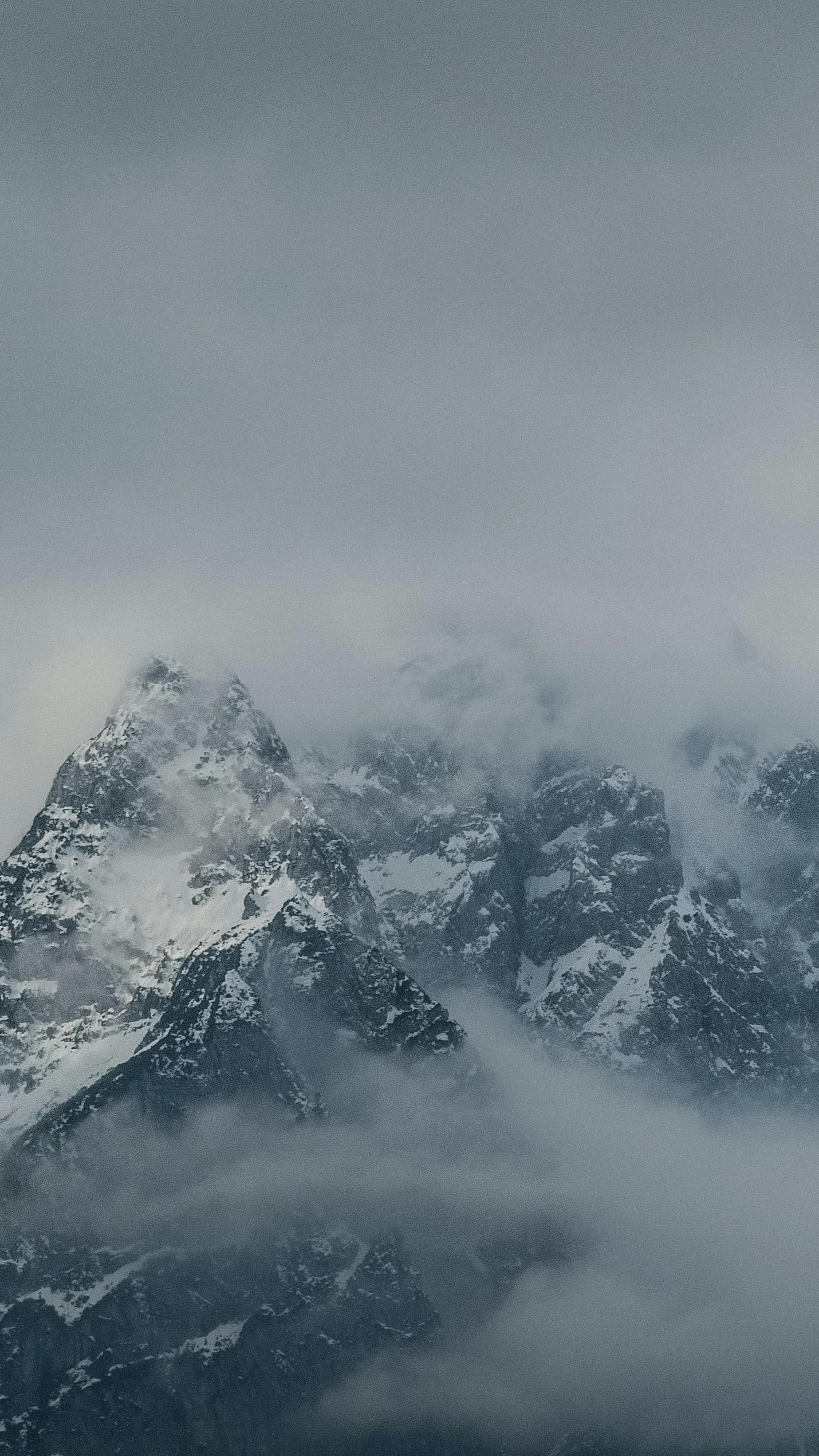 A breathtaking view of snowy mountain peaks partially covered by mist and clouds, creating a mysterious ambiance.