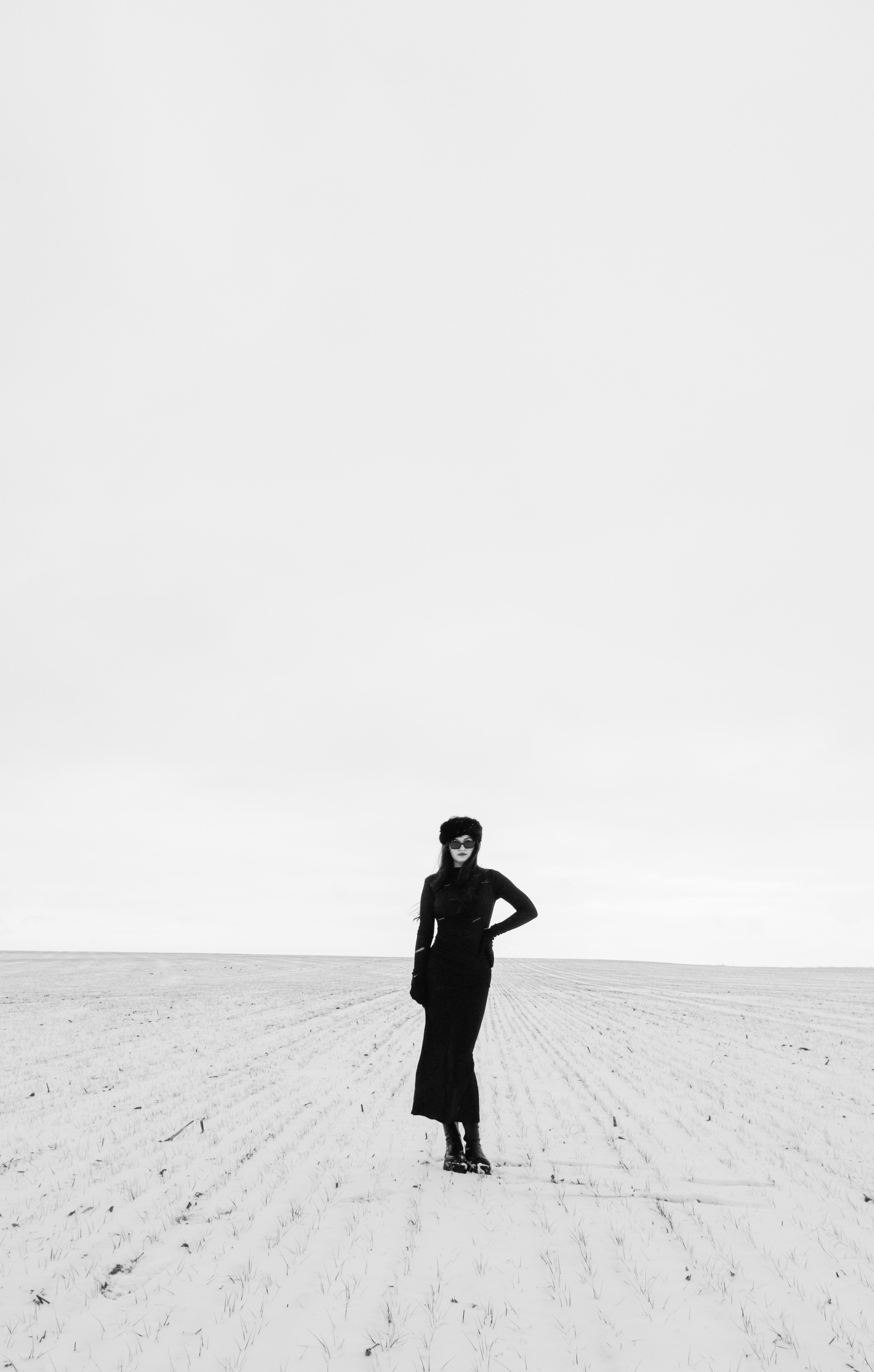 A lone figure dressed in black stands in a vast, open field under a muted sky.