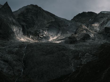 Dark and dramatic mountain landscape with moody lighting under a cloudy sky.