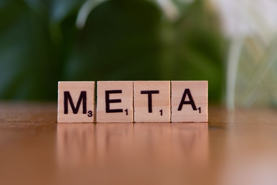 ぼやけた緑色の背景のテーブルの上に、木製の文字ブロックで「META」と書かれています。