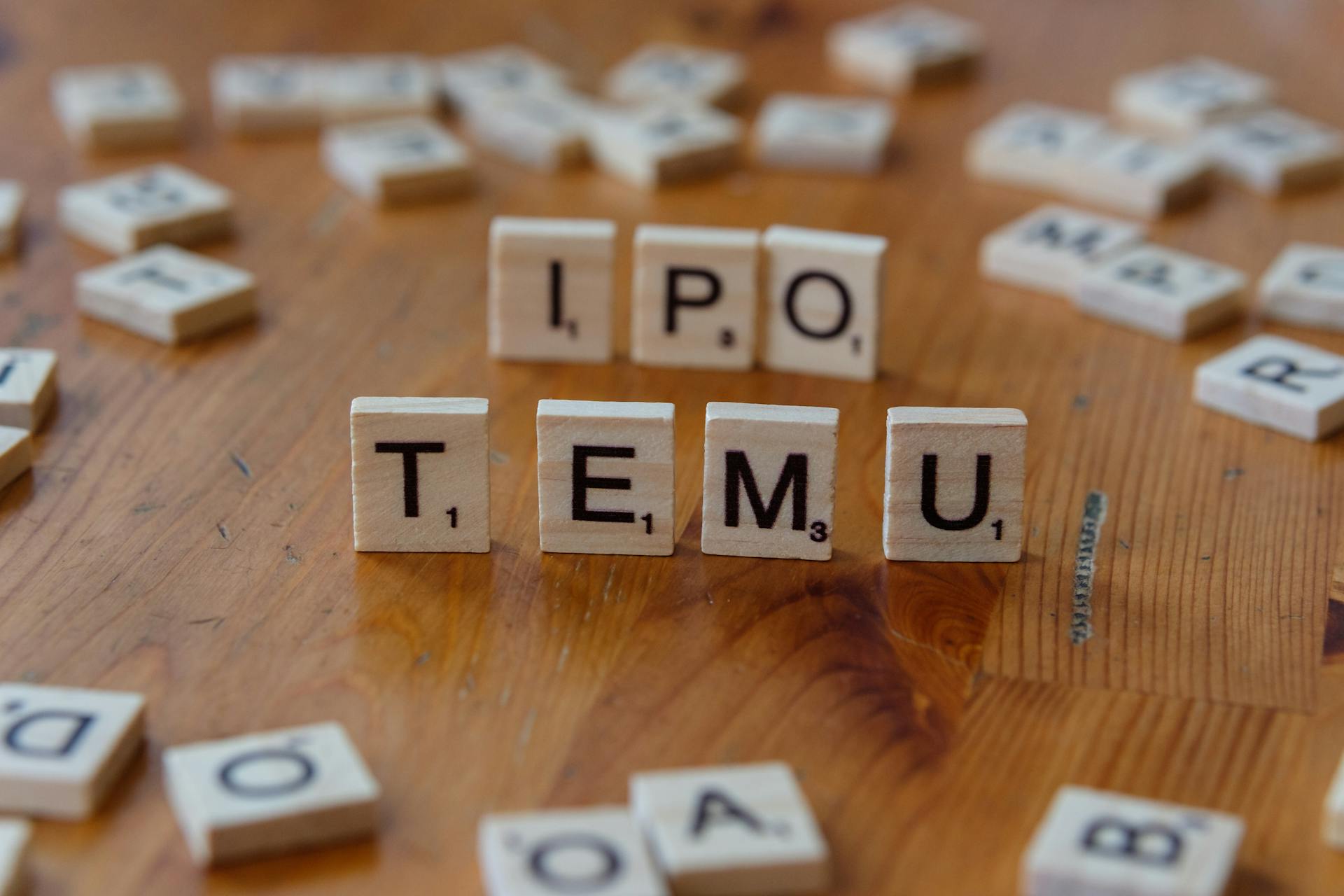 Scrabble tiles spelling IPO and Temu placed on a wooden table surface.