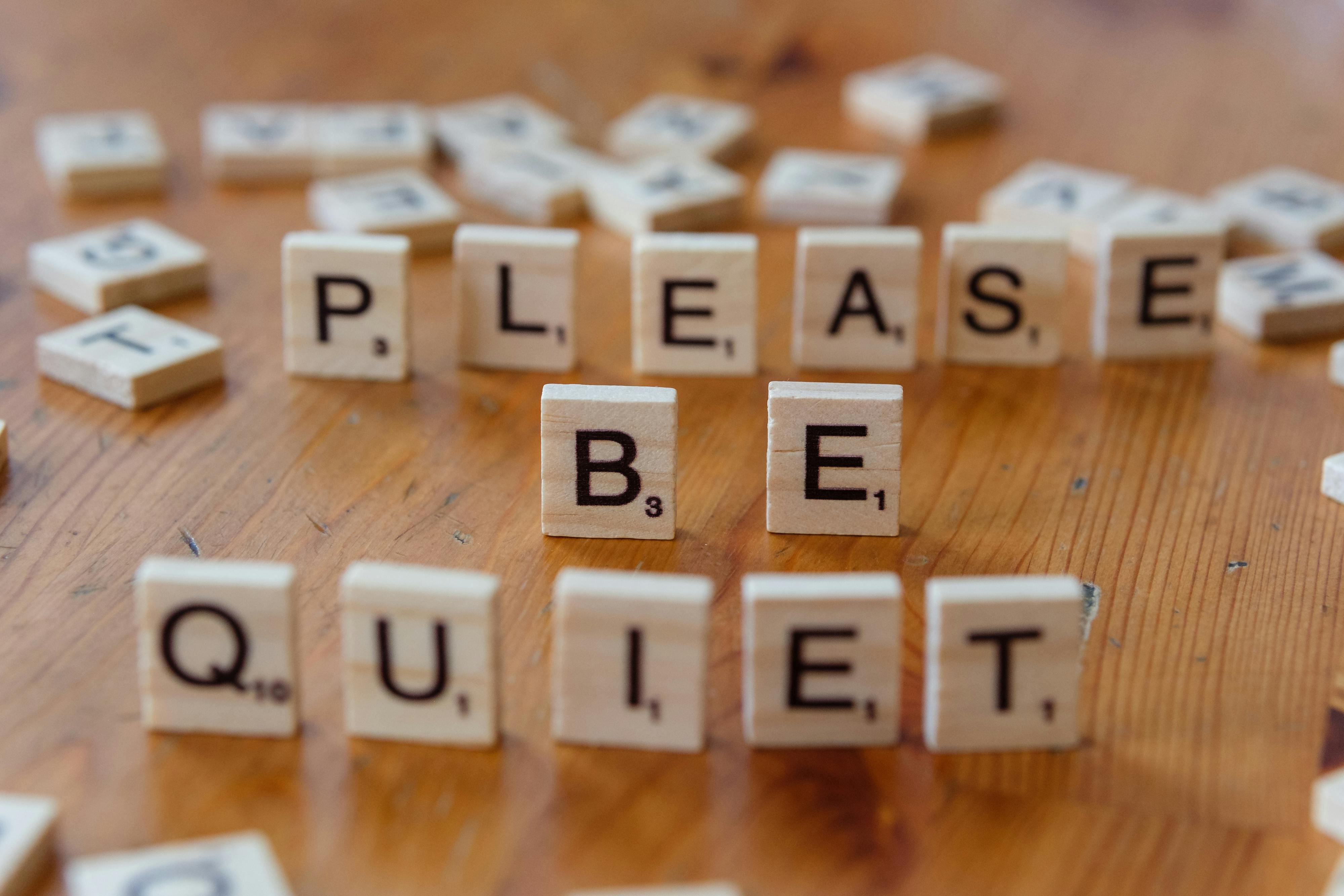 Free Scrabble tiles on a wooden table spell out 'Please Be Quiet'. Stock Photo