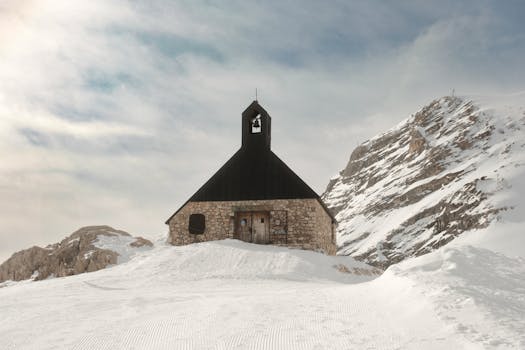 Stone chapel on Germany's Zugspitze, covered with snow under a blue sky.
