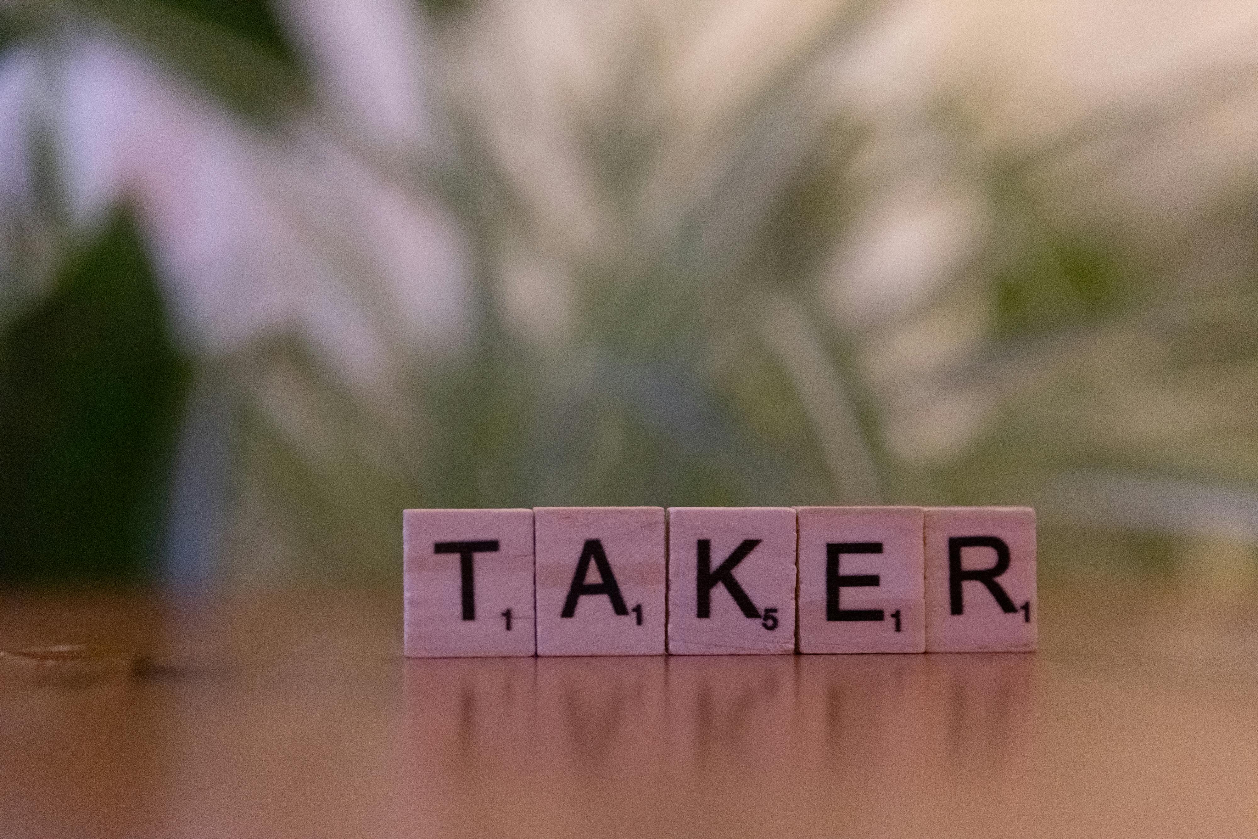 Close-up of Scrabble tiles spelling 'taker' on a blurred background, focus on letters.