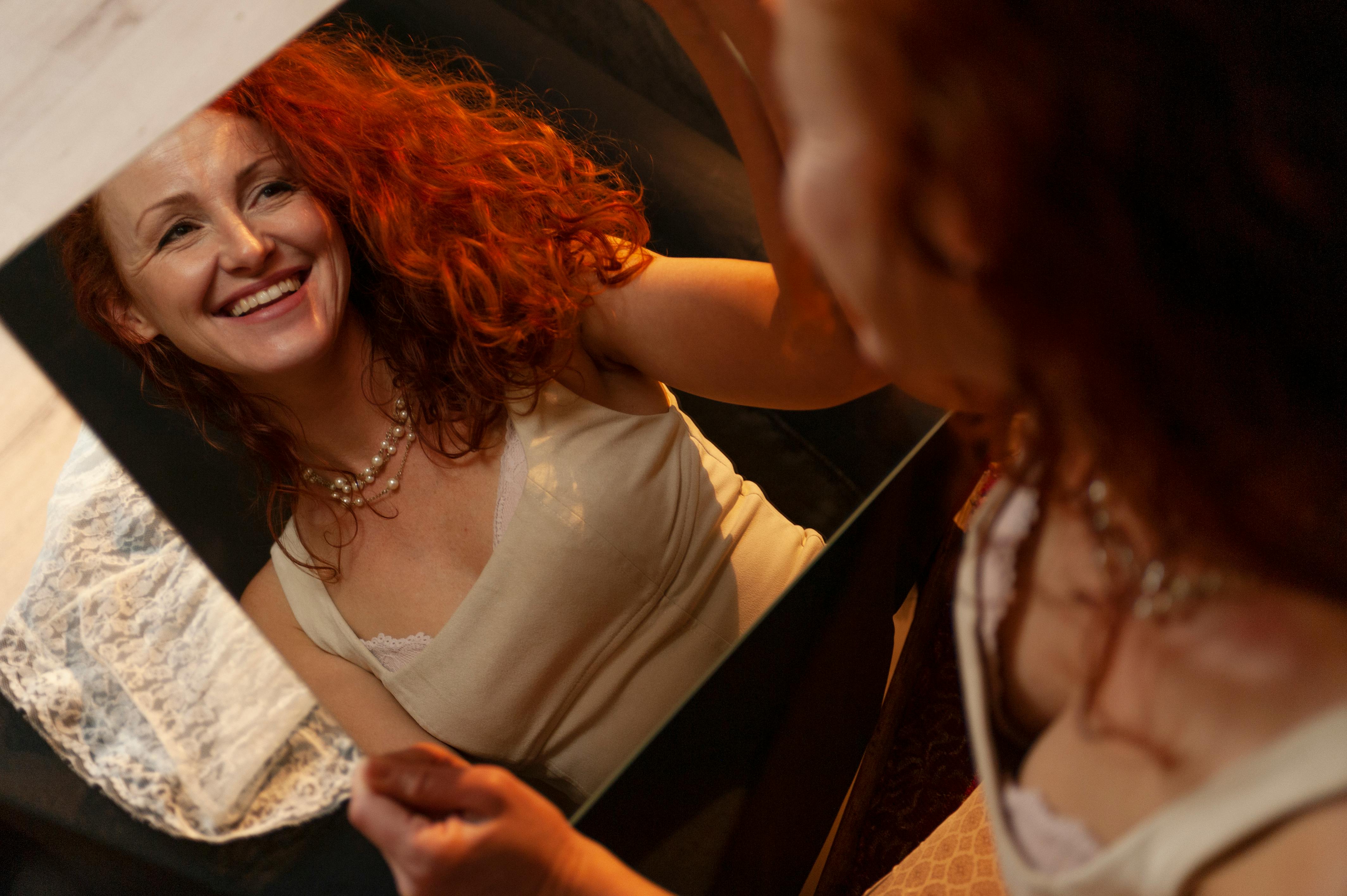 Happy woman with curly red hair smiling at her reflection in a mirror.