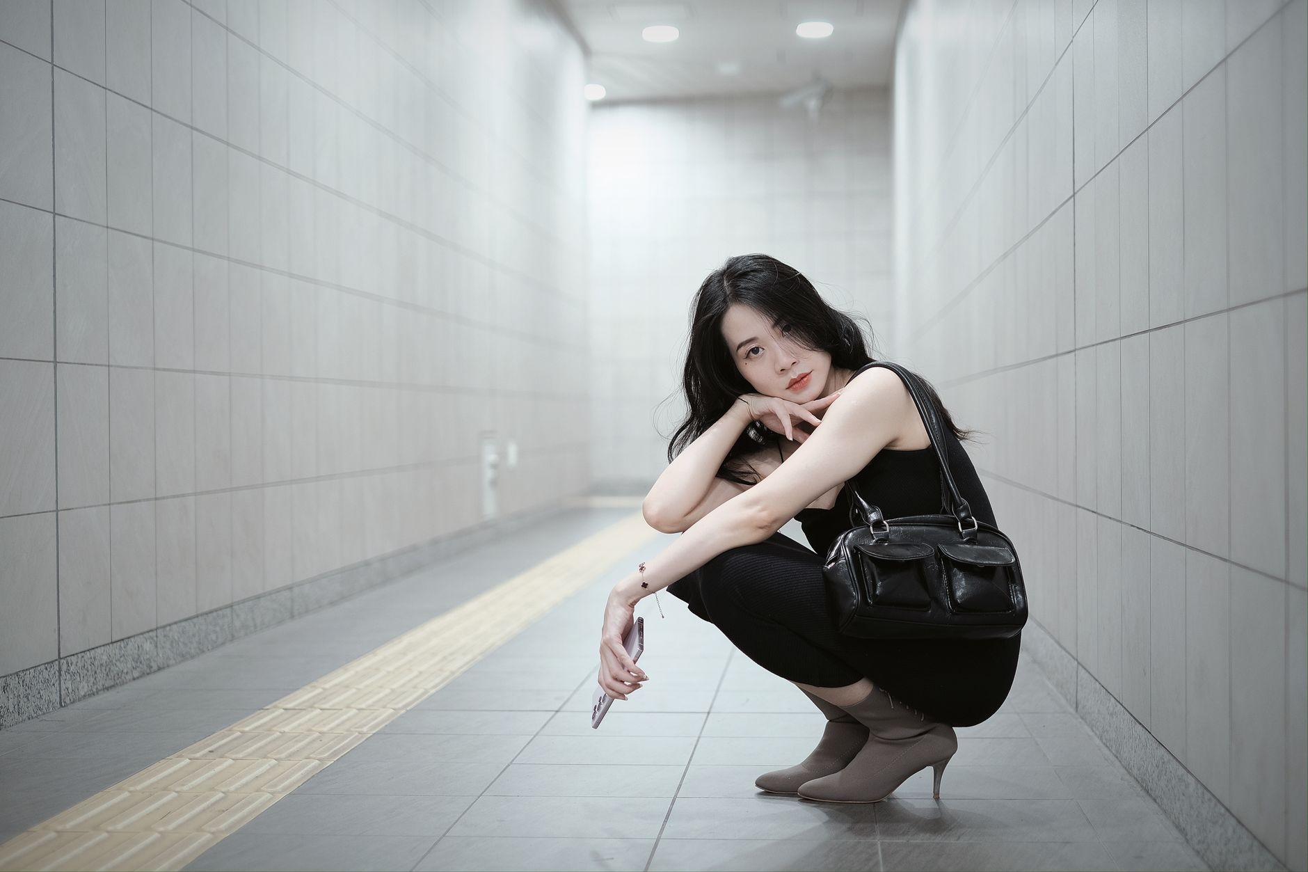 Elegant woman in black outfit poses in a modern subway tunnel.