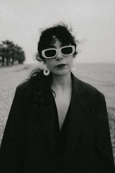 Moody portrait of a woman in sunglasses on a beach in black and white.