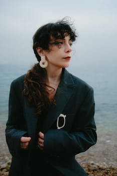 Stylish woman with curly hair in dark coat near the sea.