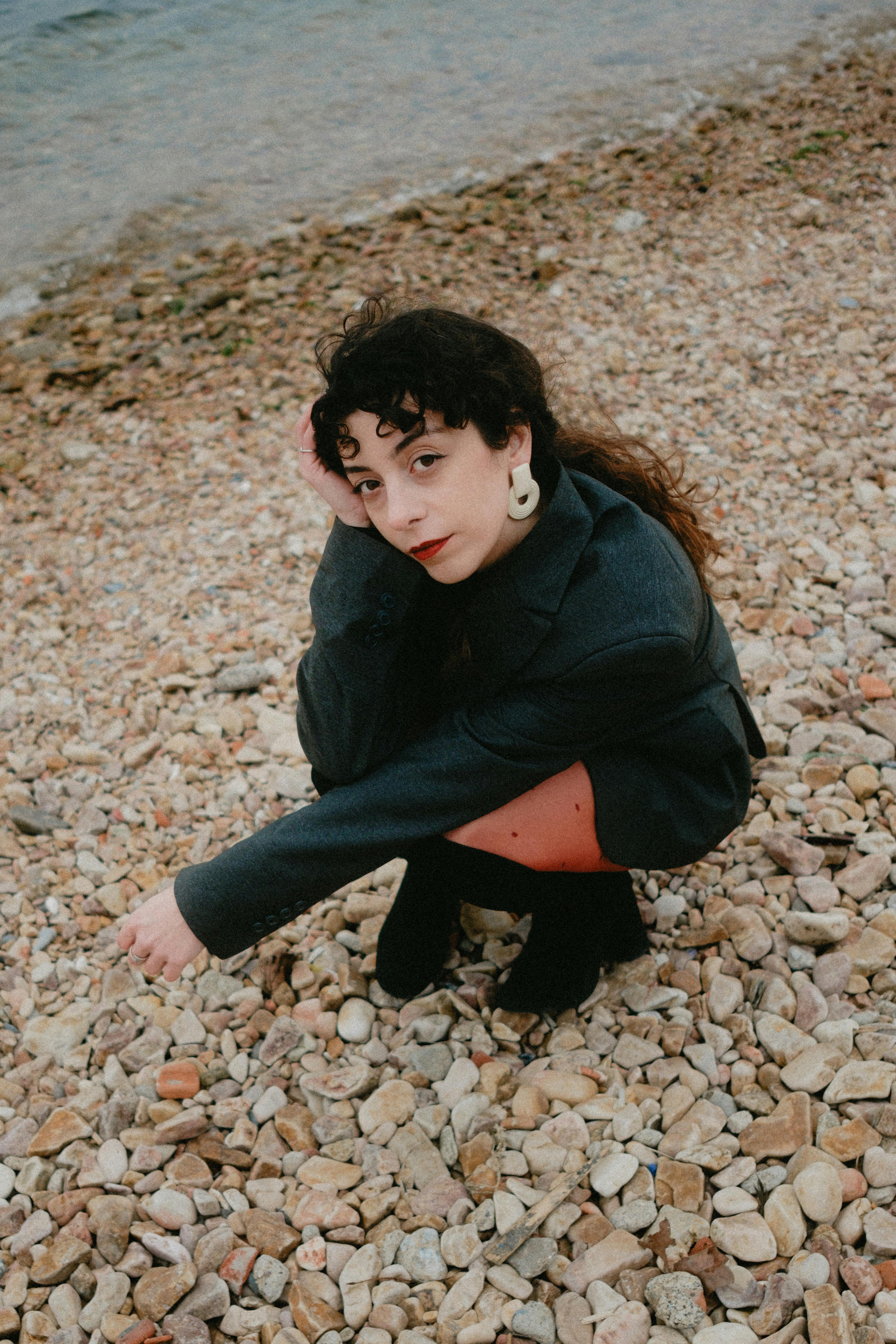 Stylish woman kneeling on a pebble beach in an elegant coat.