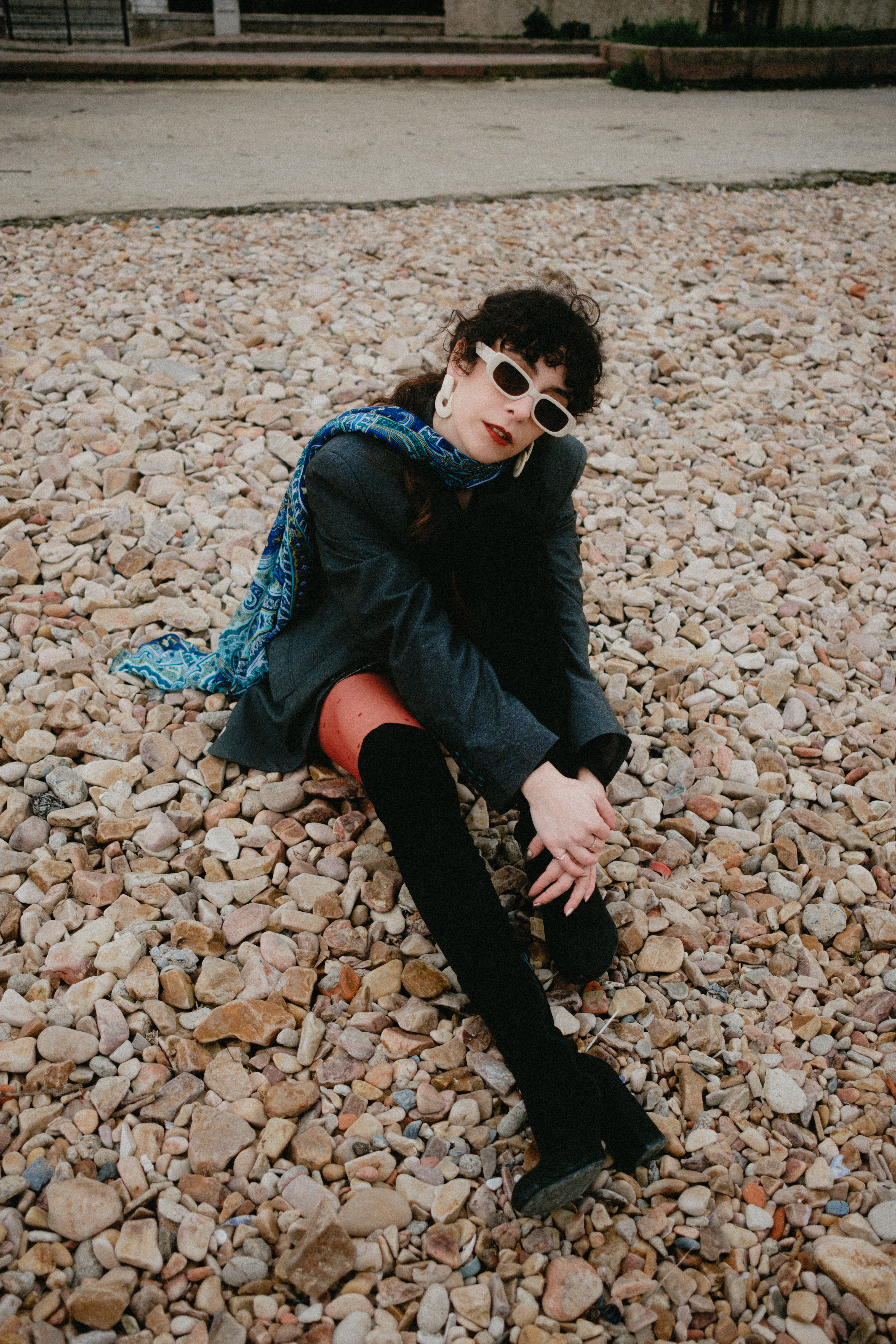 Woman in chic attire posing on a rocky beach, exuding confidence and style.