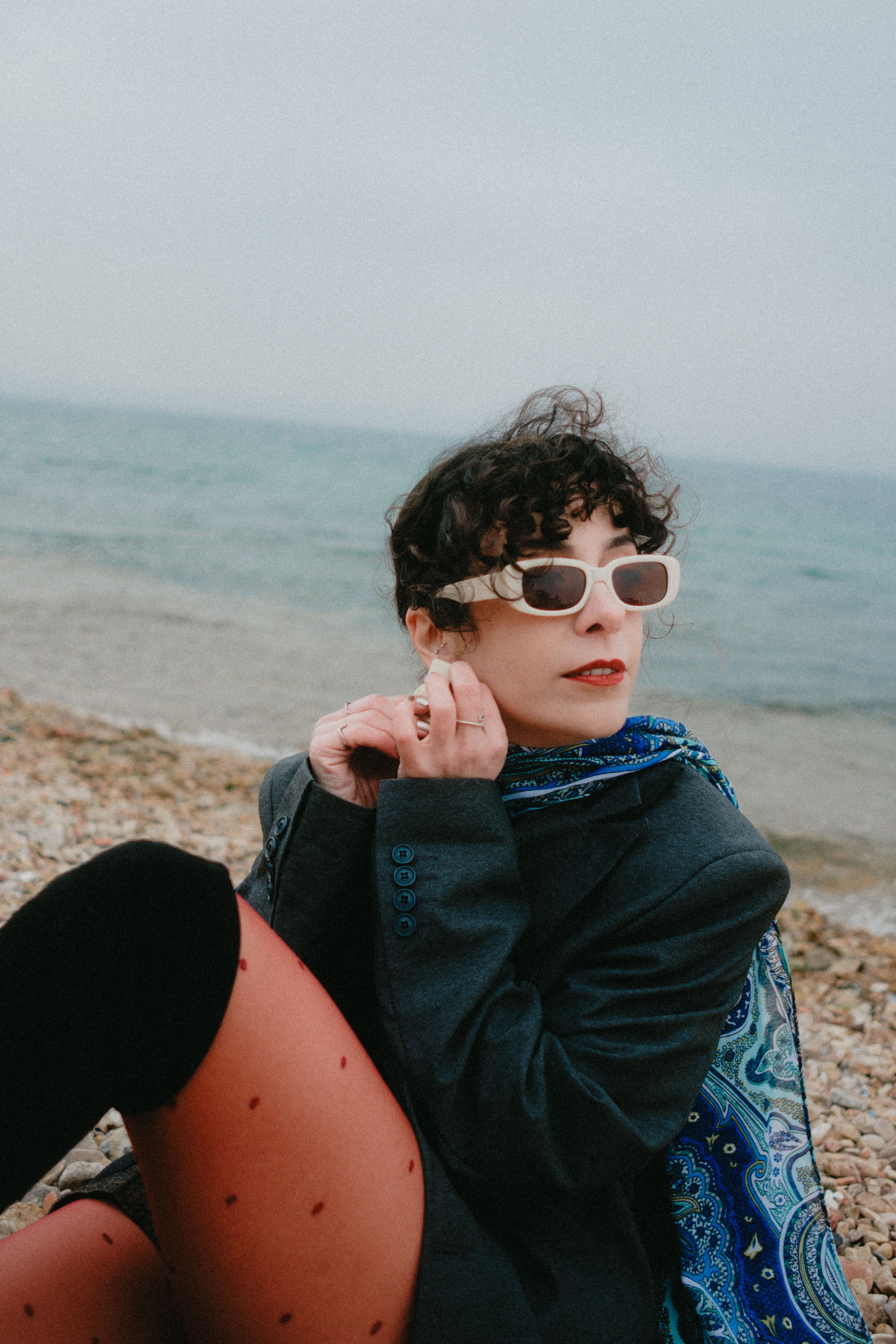 Fashionable woman with sunglasses sitting by the sea on a rocky beach.