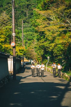 Group of Japanese students walking on a sunny street with lush greenery and mountains in the background.