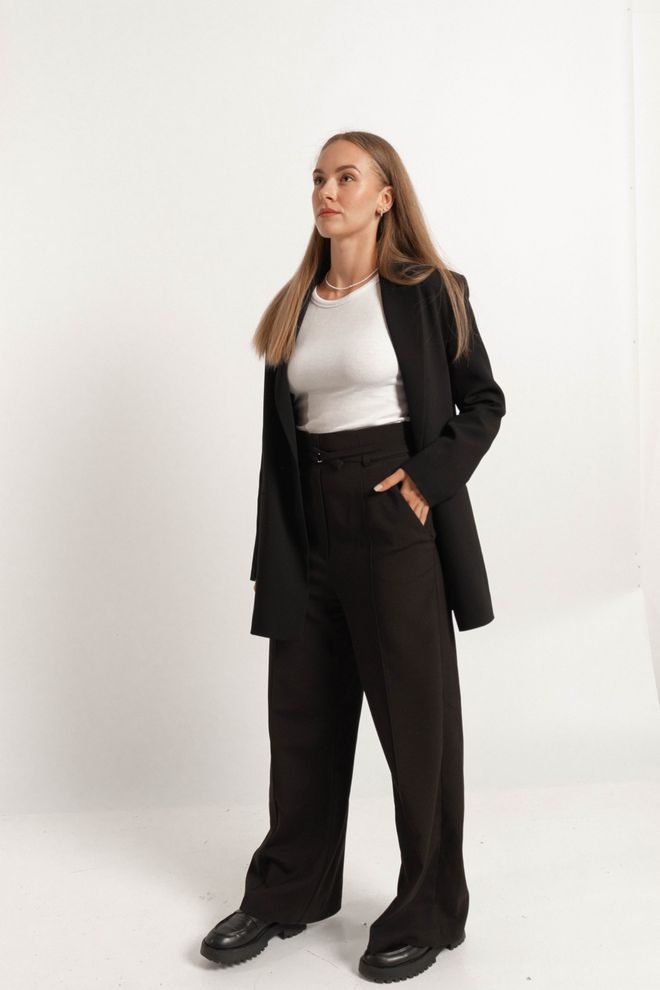 Creator in a black tailored blazer and straight-leg trousers on a pale studio backdrop — Даша Михальченко on Pexels