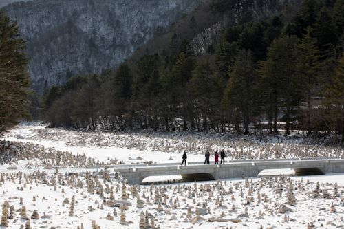 Free A picturesque winter scene of a snowy landscape with cairns, a bridge, and four people crossing. Stock Photo