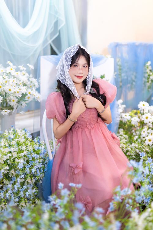 Free A young woman in a pink dress sits elegantly amid lush white flowers. Stock Photo