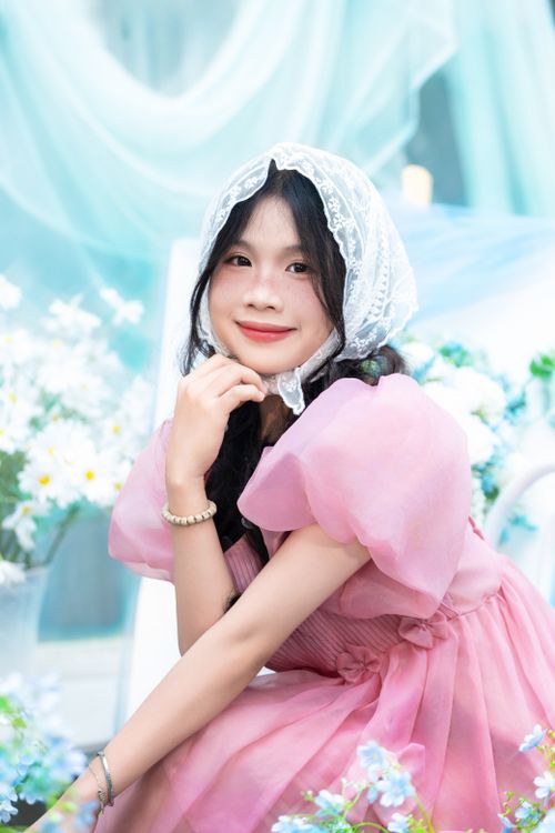 Free Smiling young woman in a pink dress and lace bonnet surrounded by flowers. Stock Photo