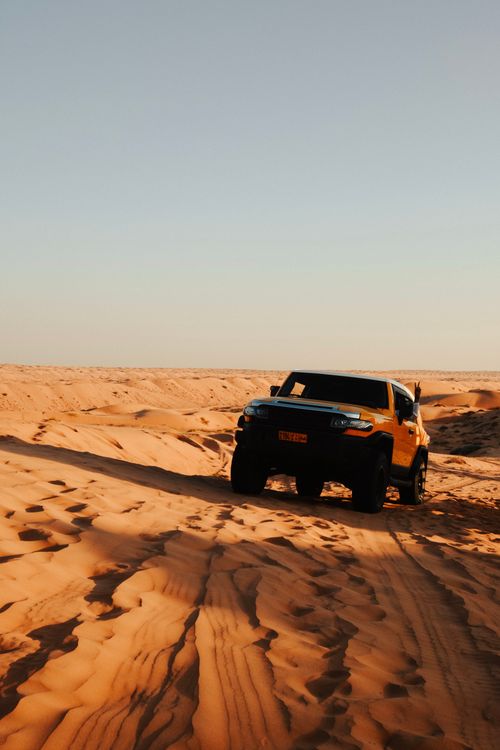 Free An SUV navigating the vast Umman desert dunes under a clear sky, perfect for off-road enthusiasts. Stock Photo
