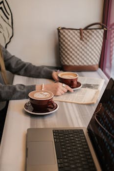 A warm coffee shop ambiance featuring laptops, lattes, and newspapers, ideal for work or relaxation.