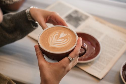 Free Warm coffee latte art with open newspaper in cozy indoor setting. Stock Photo