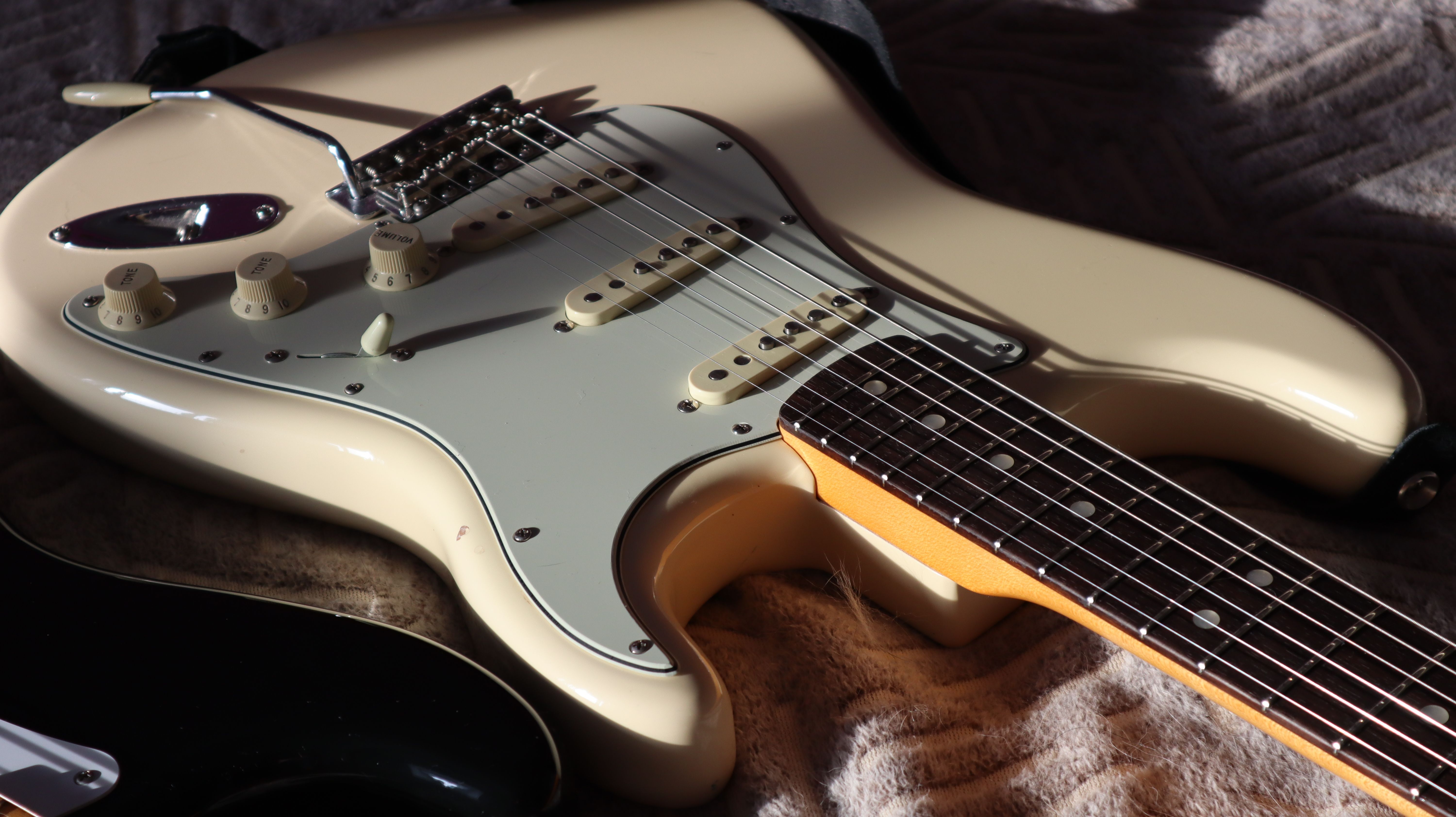 Detailed close-up of a cream Stratocaster electric guitar highlighting strings and body.