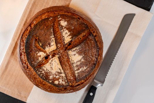 Close-up of a freshly baked artisan sourdough bread loaf with a rustic crust on a cloth with knife.