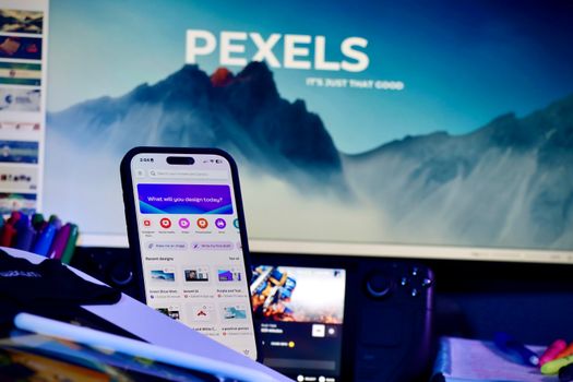 A creative workspace with a smartphone displaying design apps and a large monitor in the background.