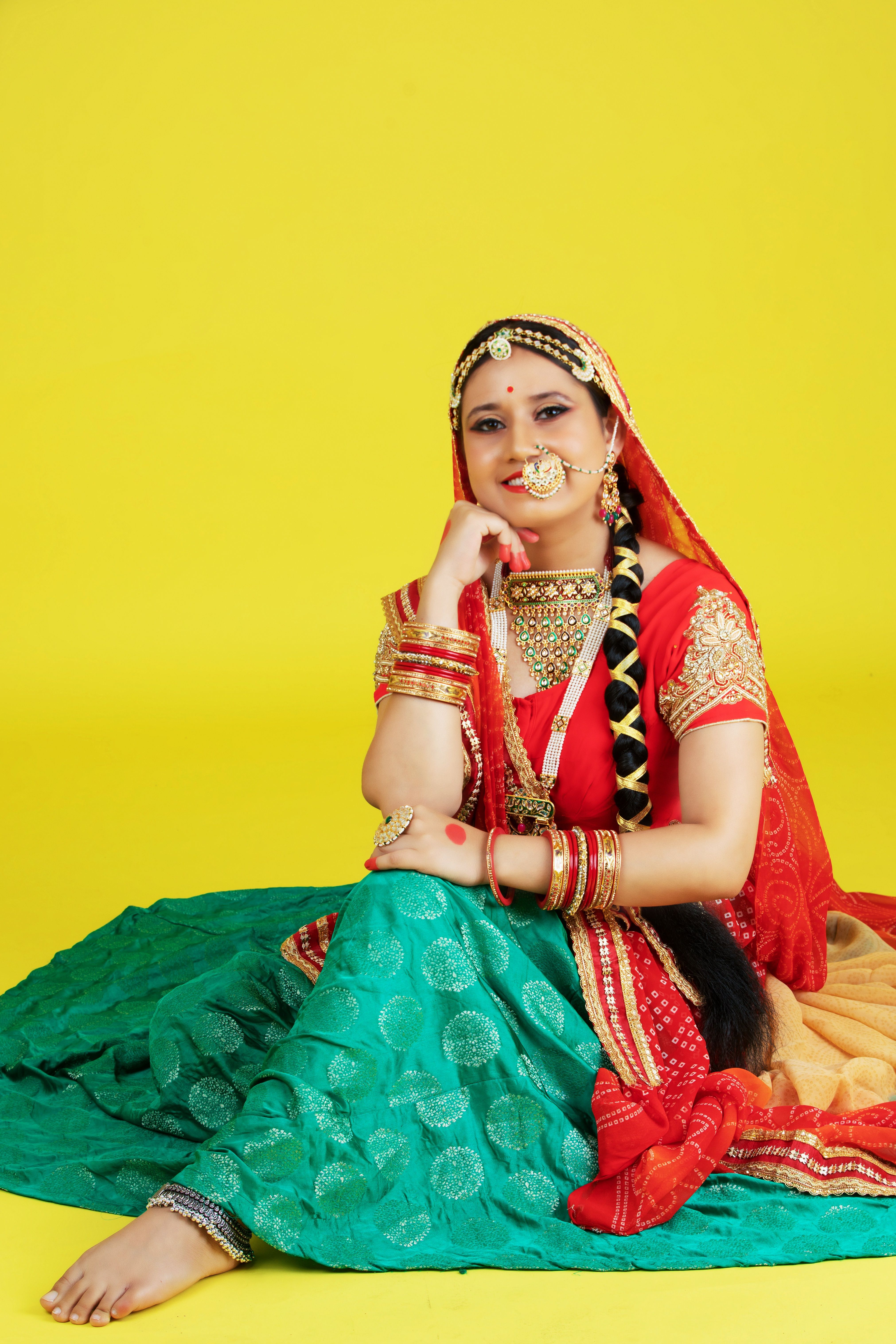 Indian woman dressed in traditional Rajasthani attire, posing confidently against a yellow backdrop.