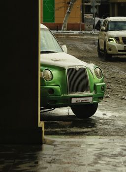 A vibrant green retro car partially visible on a snowy city street corner.