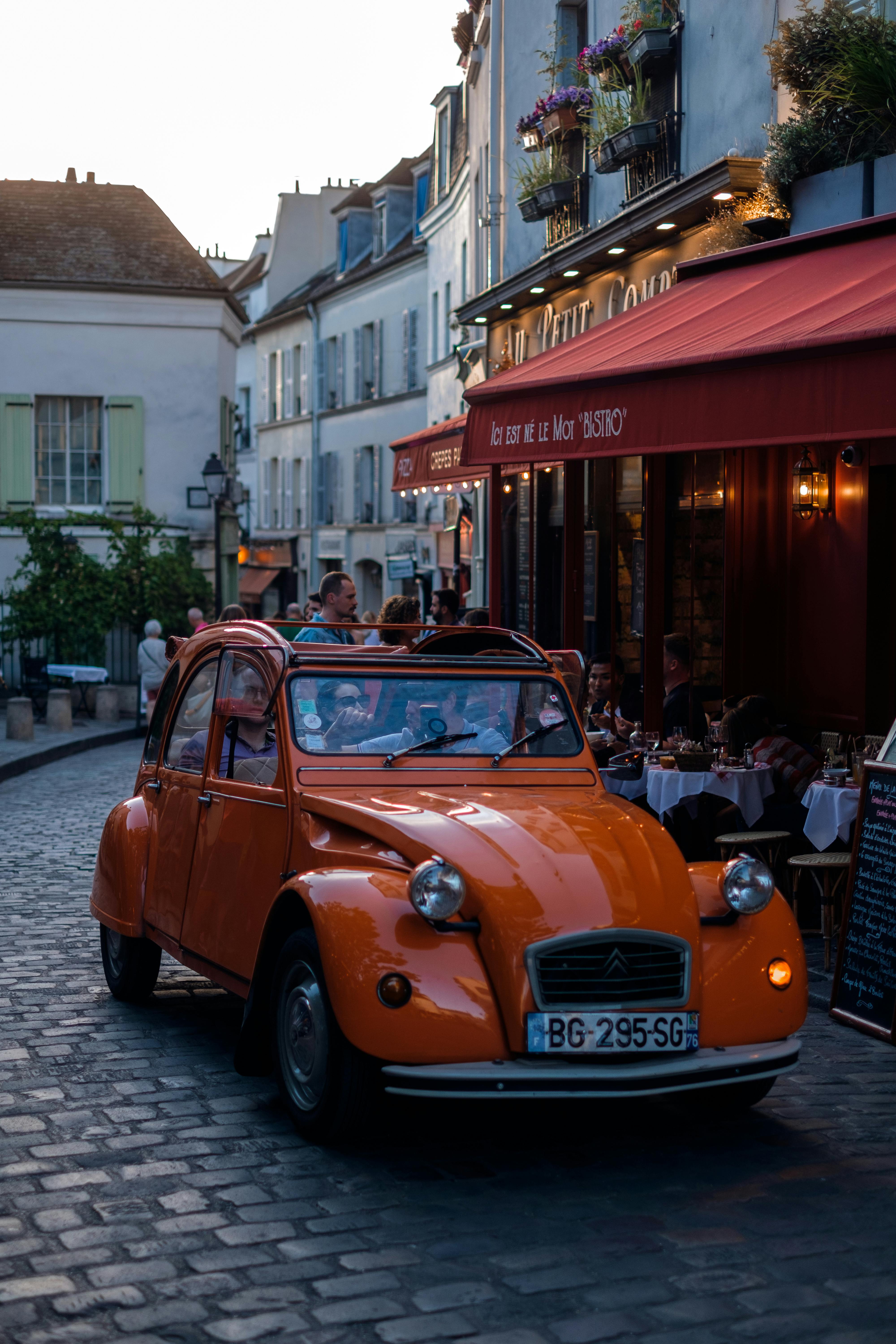 Charming Paris street scene with a vintage orange car near a cozy bistro at dusk.