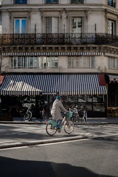 A cyclist rides past a traditional Parisian café with striped awnings on a sunny day.