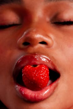 Artistic close-up portrait of a woman's lips holding a ripe strawberry.