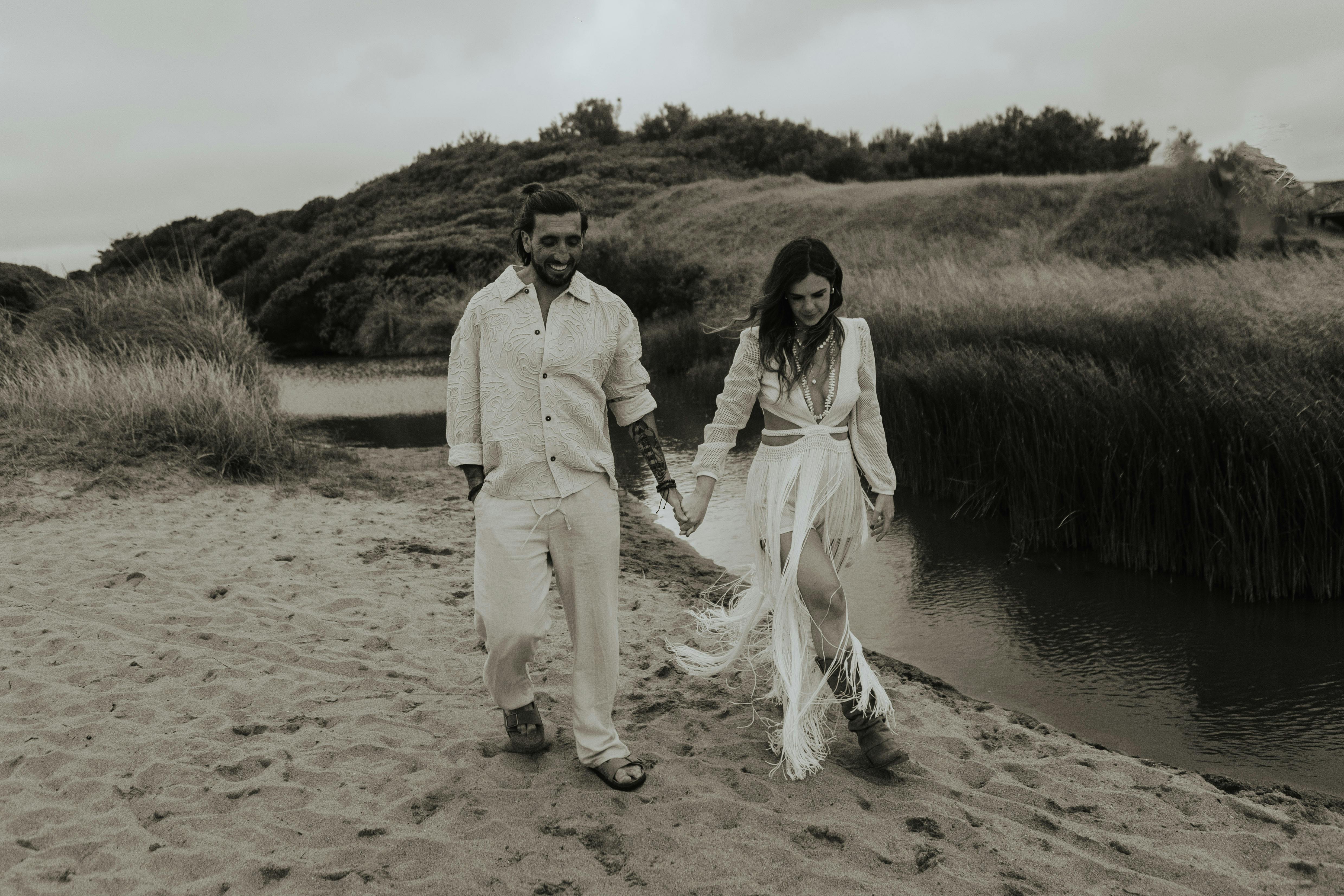 Couple walking hand in hand by a river, embracing love and tranquility in a lush, serene setting.