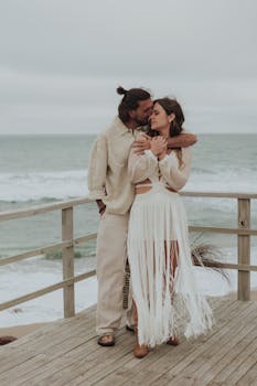 A loving couple embraces on a beachfront deck with ocean views, capturing a serene moment.