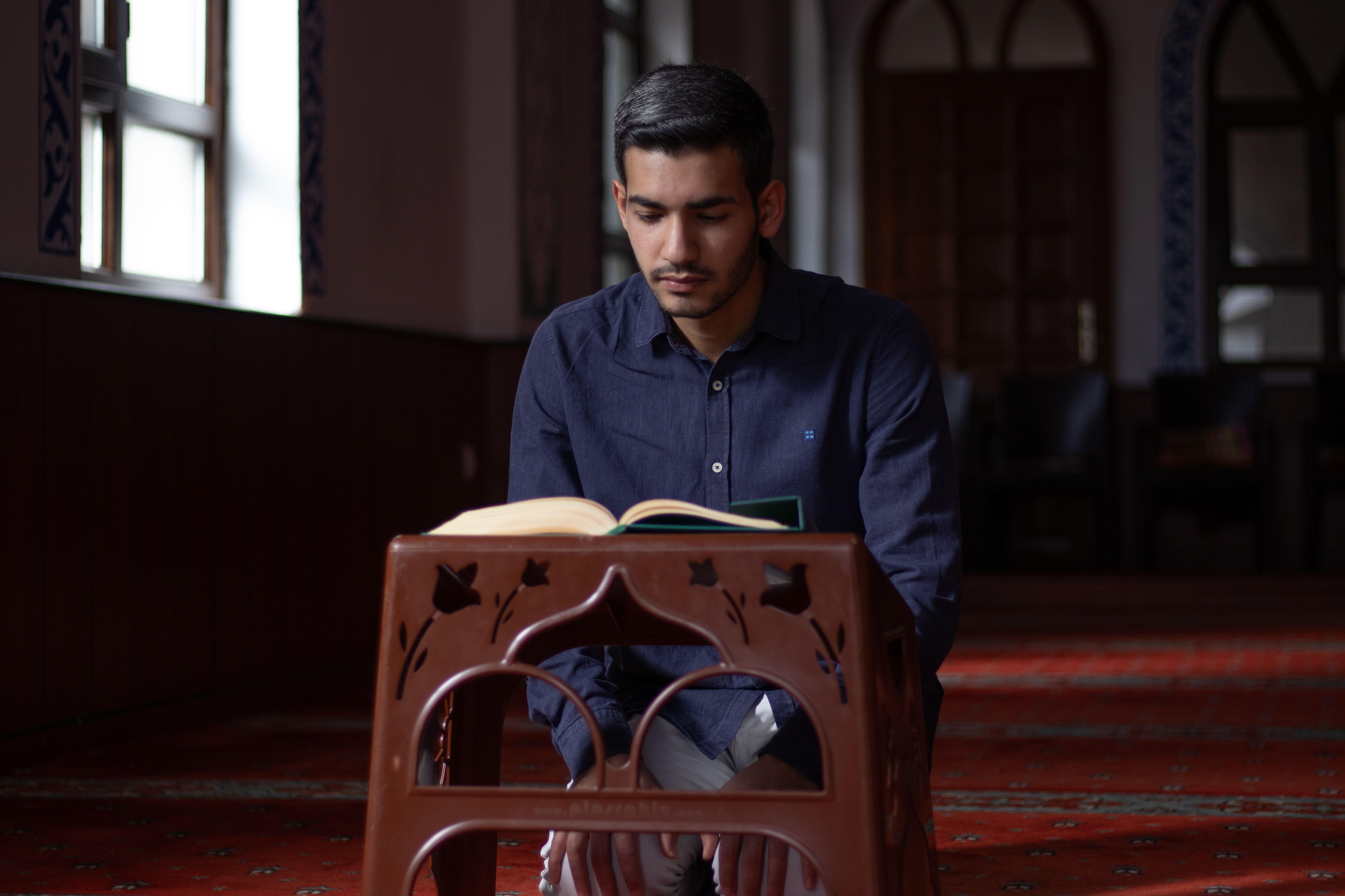 A young man praying and reading in a serene mosque interior.