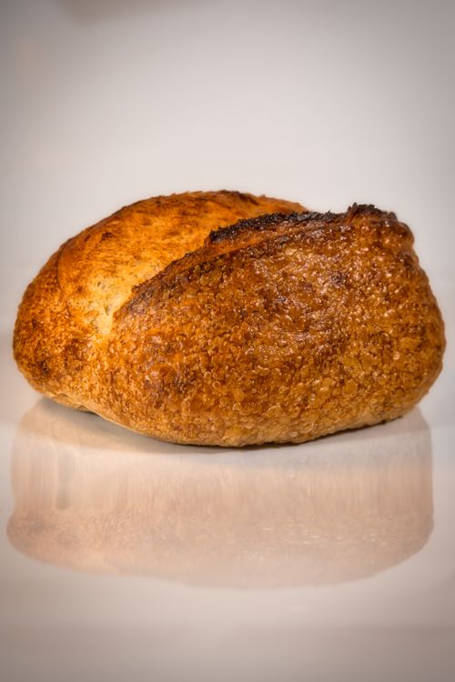 Free Golden crusted artisan bread loaf displayed on a reflective surface, showcasing its texture and color. Stock Photo
