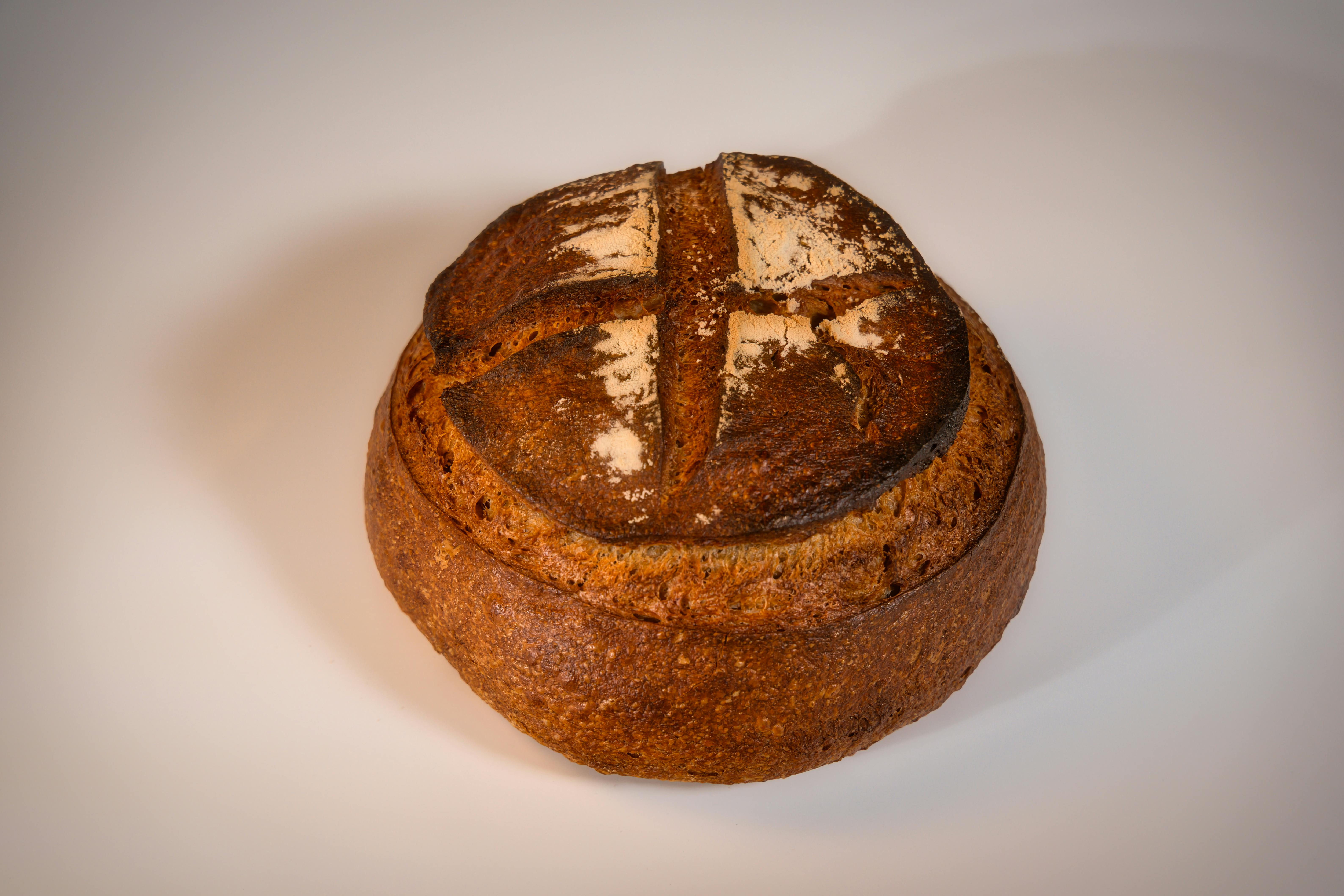 Close-up of a crusty artisanal bread loaf with a cross pattern on a white surface, highlighting its rustic texture.
