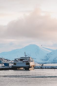 A boat docked at Tromsø harbor, surrounded by snowy mountains and winter landscape.