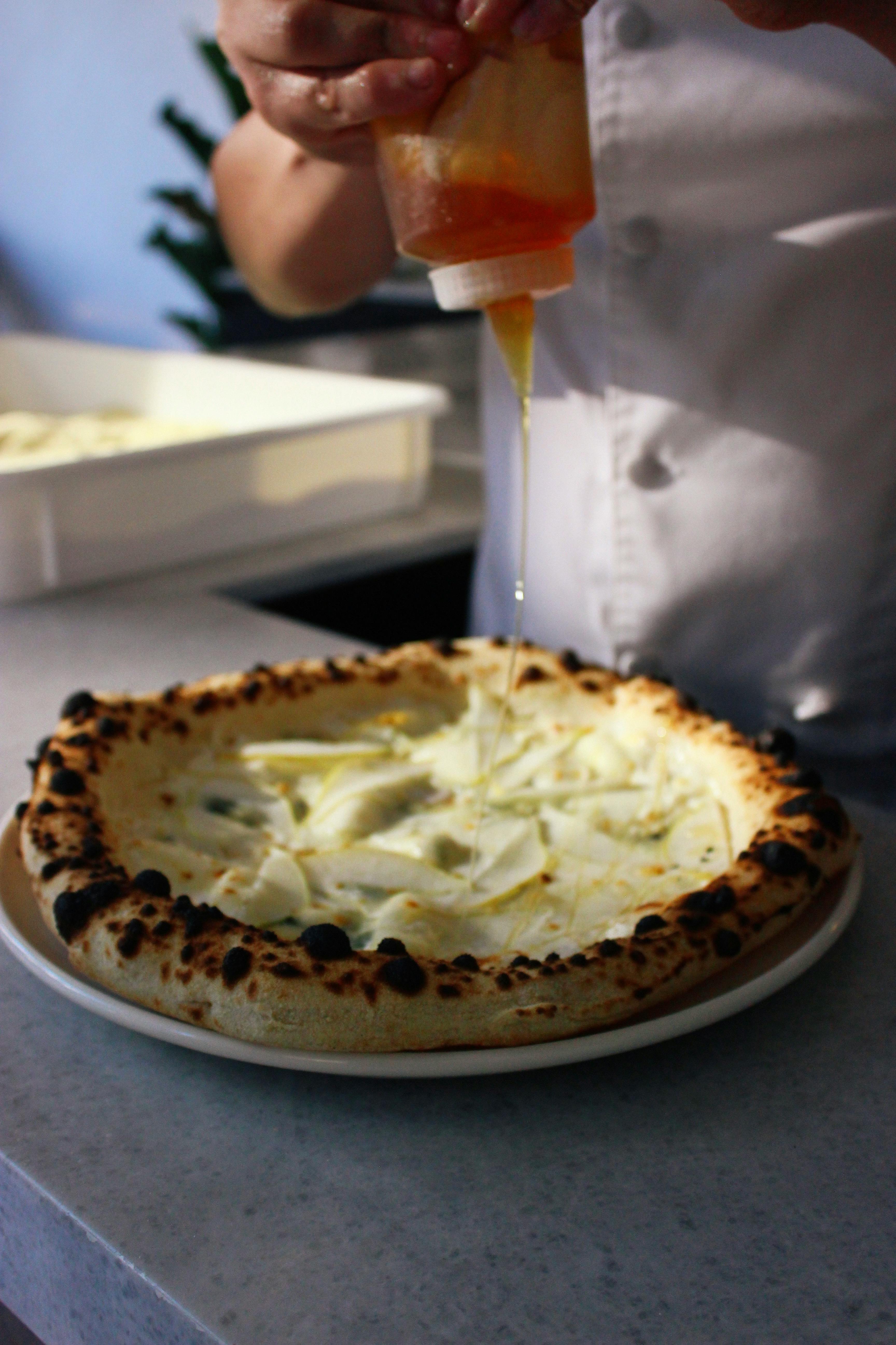 A chef adds finishing touches with oil to a freshly baked pizza.