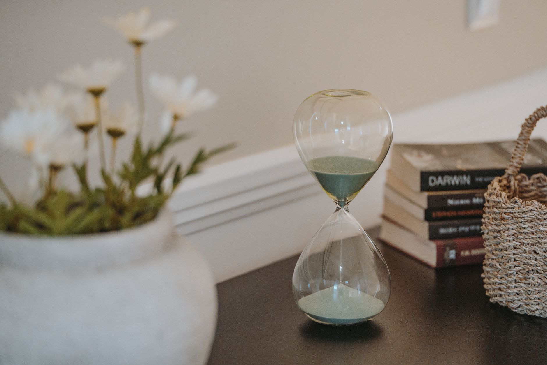 A serene interior with an hourglass, books, and decorative flowers in focus, creating a calm atmosphere.