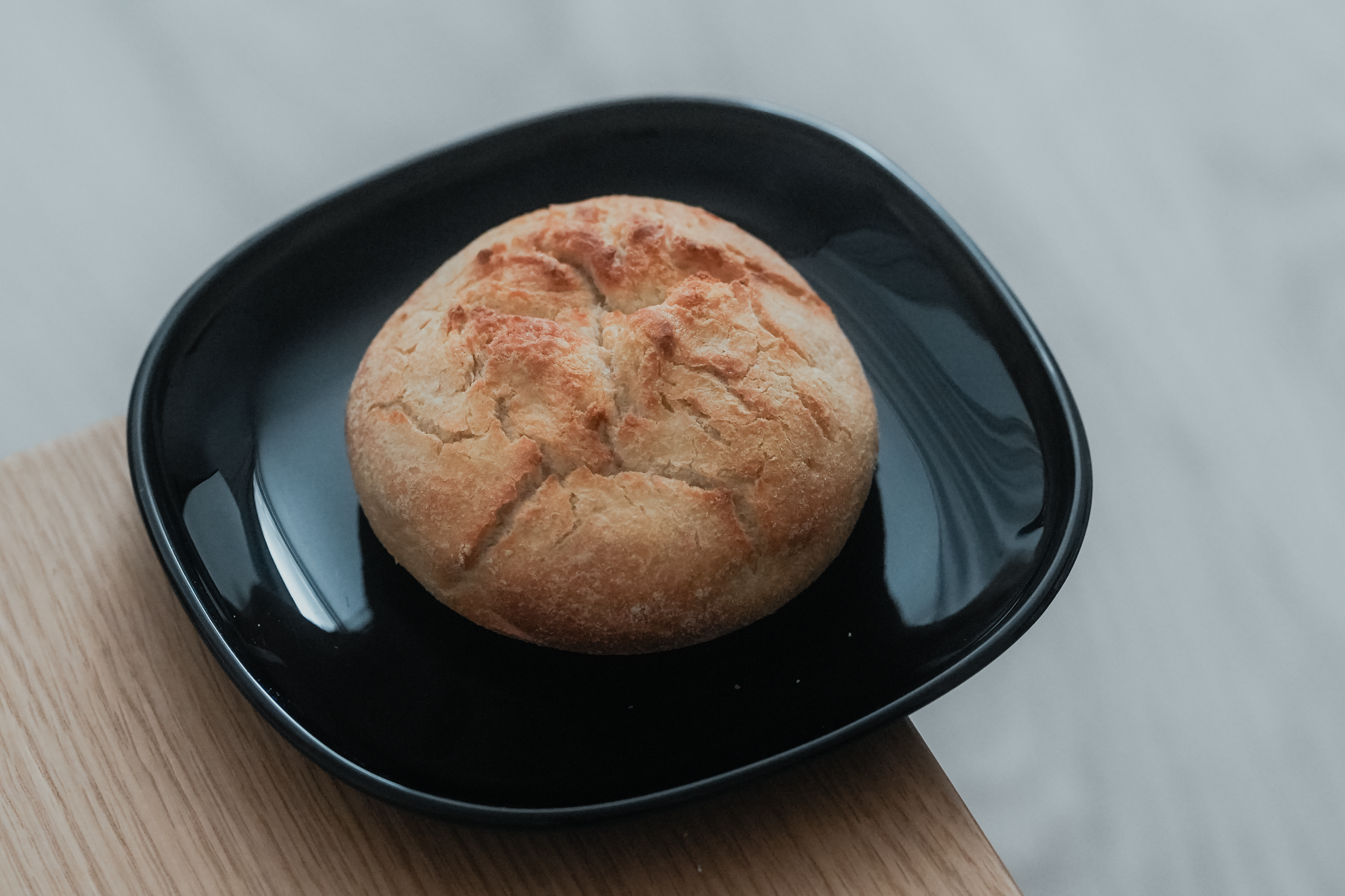 A freshly baked round bread roll on a black plate, perfect for food photography.