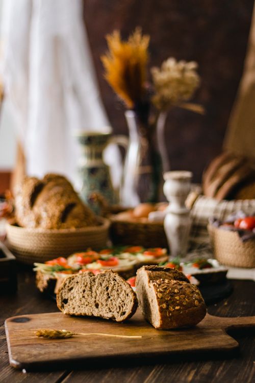 Free Rustic bread on wooden board surrounded by Mediterranean style table setting with bread and vegetables. Stock Photo