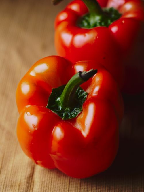 Free Close-up of fresh red bell peppers on a rustic wooden surface, highlighting their vibrant color and texture. Stock Photo
