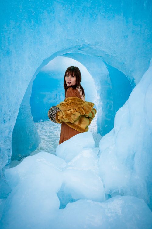 Free Woman in vibrant winter attire poses in an icy tunnel, combining fashion with snowy nature. Stock Photo