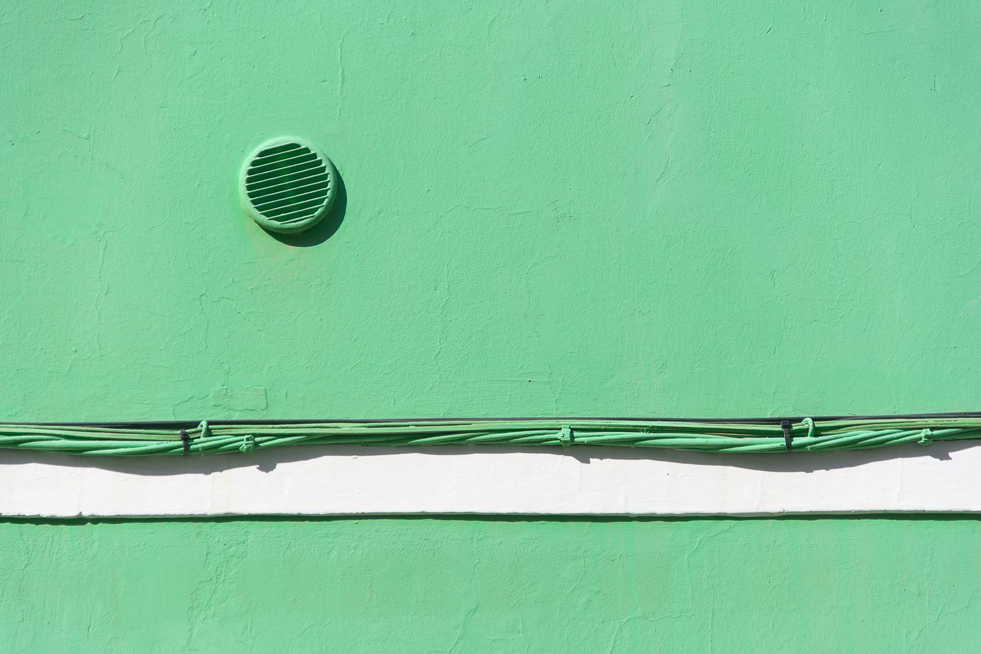 Green wall with a vent and horizontal wires, displaying minimalistic design.