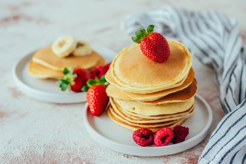 Free Stacks of fluffy pancakes garnished with ripe strawberries, bananas, and raspberries on a stylish plate. Stock Photo