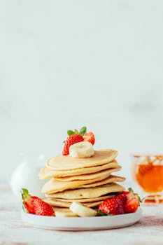 Tasty stack of pancakes adorned with fresh strawberries and banana slices, perfect breakfast delight.