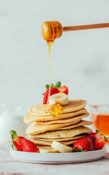 Mouthwatering stack of pancakes with honey drizzling, strawberries, and bananas. Perfect breakfast setting.