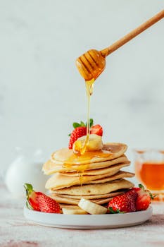 Stack of pancakes topped with fresh strawberries and honey drizzle, perfect for a sweet breakfast.