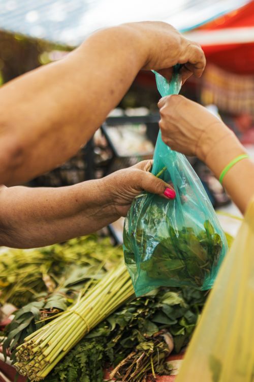 Free A close-up of a fresh produce exchange at an outdoor market with hands exchanging a bag of greens. Stock Photo